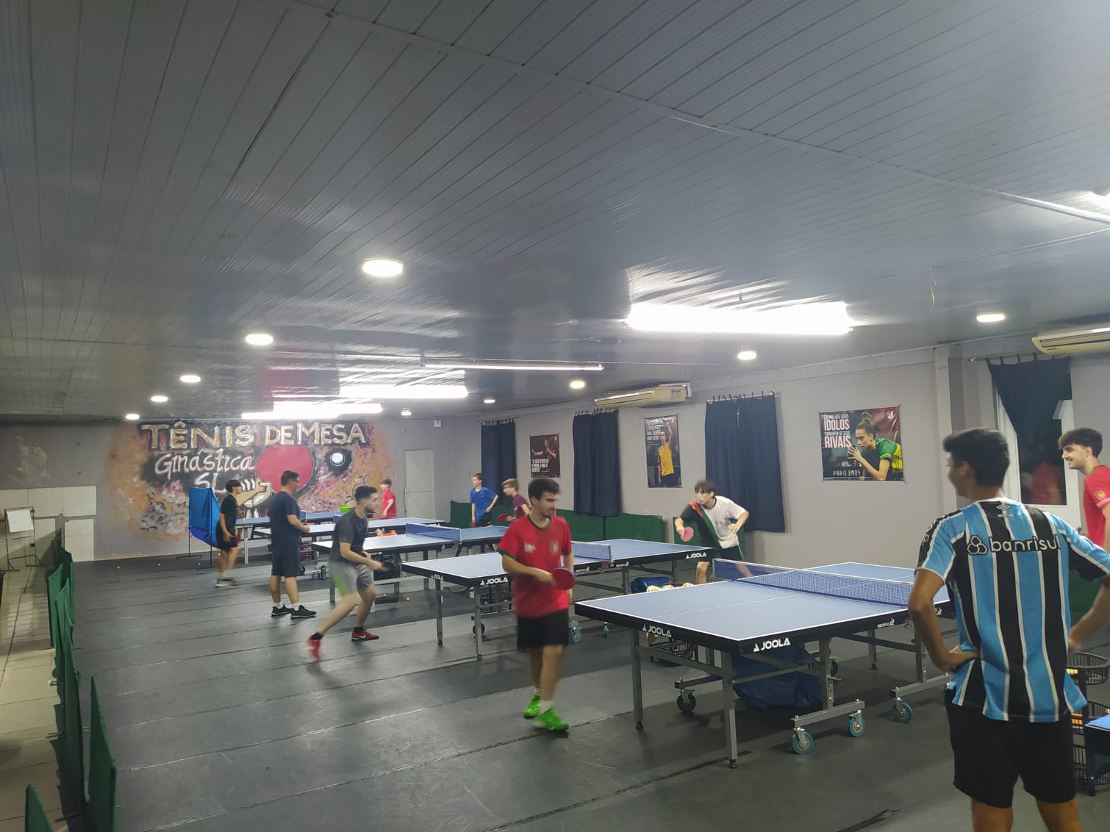 Visão ampla da sala com mesas e alunos treinando