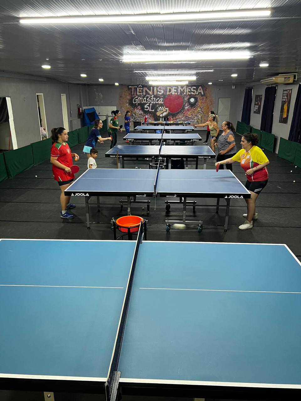 Turma jogando tênis de mesa no espaço com piso emborrachado